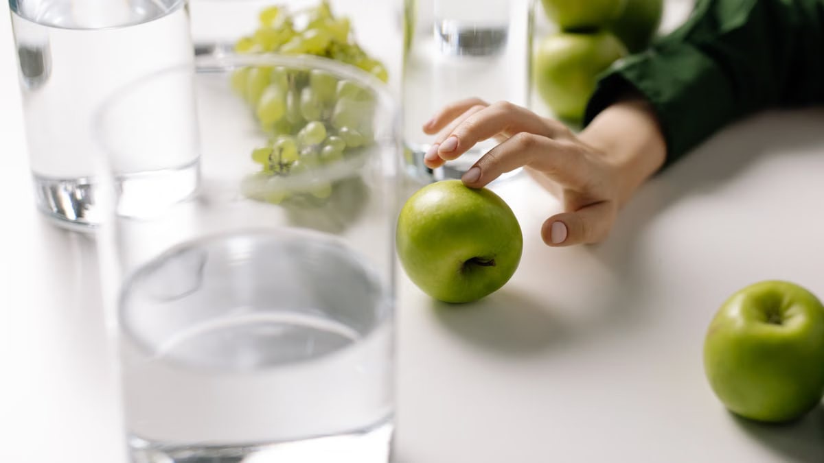 Refreshing image of green apples and grapes with glasses of water on a table, promoting healthy living.